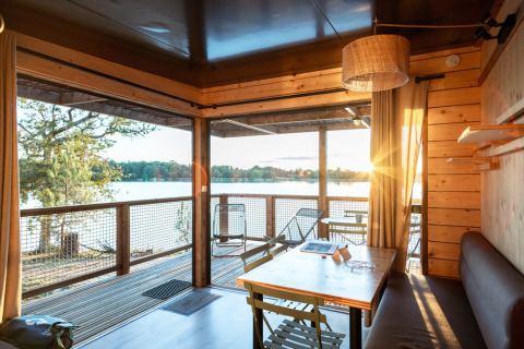 Cabaña moderna de madera con vista al lago al atardecer en Huttopia Lac de l’Uby - Gers, Occitanie, Francia.
