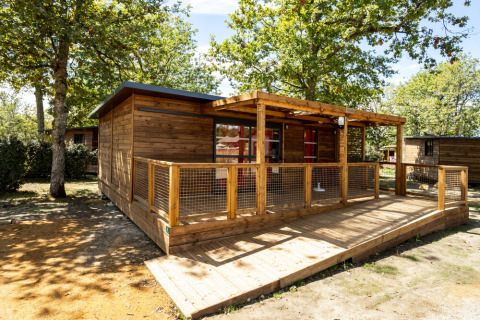 Gemütliches Holzhaus mit überdachter Terrasse im Grünen, aufgenommen im Huttopia Lac de l'Uby - Gers, Frankreich.