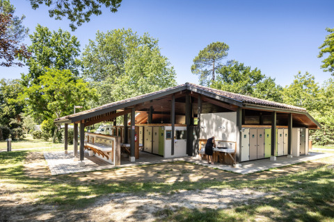 Edificio sanitario al aire libre en Huttopia Lac de l'Uby - Gers, rodeado de árboles en Occitanie, Francia.