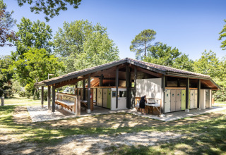 Edificio sanitario al aire libre en Huttopia Lac de l'Uby - Gers, rodeado de árboles en Occitanie, Francia.