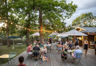 Buitenterras bij Huttopia Lac de l'Uby - Gers, Frankrijk, met mensen die genieten onder lichtslingers.