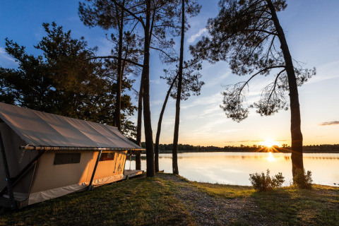 Tienda junto al lago entre árboles al atardecer en Huttopia Lac de l'Uby, parque de vacaciones en Occitania, Francia.