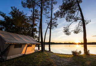 Tent aan het meer tussen bomen bij zonsondergang in Huttopia Lac de l'Uby, een vakantiepark in Occitanië, Frankrijk.