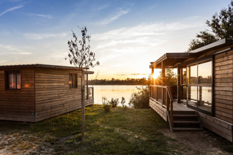 Cabañas de madera junto al lago al atardecer en Huttopia Lac de l'Uby - Gers, parque vacacional en Occitania, Francia.