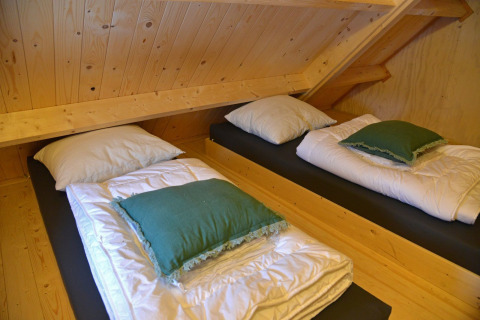 Two single beds under a slanted wooden ceiling in the Ooievaarsnest tree house at Camping de Koeksebelt, Netherlands.