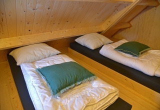Dos camas individuales bajo un techo inclinado en la casa del árbol Ooievaarsnest en Camping de Koeksebelt, Países Bajos.