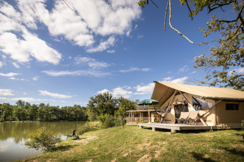 Tienda glamping junto al lago en Huttopia Lac de l'Uby, Gers, Occitania, Francia, bajo un cielo soleado.