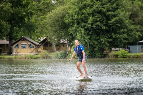 Hombre en tabla de surf eléctrica en el lago del parque vacacional Huttopia Lac de l'Uby - Gers, Occitania, Francia.