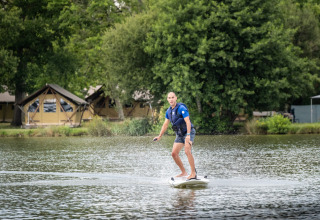 Uomo su tavola da surf elettrica sul lago al villaggio Huttopia Lac de l'Uby - Gers in Occitania, Francia.