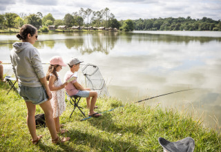 Familie ved bredden af en sø fisker ved Huttopia Lac de l'Uby - Gers feriepark i Occitanie, Frankrig.