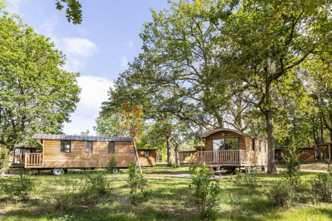 Wooden cabins set among trees at Huttopia Lac de l'Uby - Gers, a holiday park in Occitanie, France.