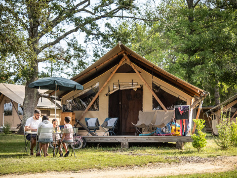 Familia sentada frente a una tienda de glamping en Huttopia Lac de l'Uby - Gers, parque vacacional en Occitania, Francia.