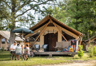 Familie sidder udenfor et glampingtelt i Huttopia Lac de l'Uby - Gers feriepark, Occitanie, Frankrig.