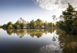 Weerspiegeling van bomen en huisjes aan het meer bij Huttopia Lac de l'Uby - Gers, Occitanië, Frankrijk.