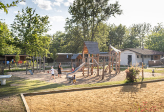 Parco giochi con bambini e adulti a Huttopia Lac de l'Uby, Occitania, Francia, vicino a casette in legno.