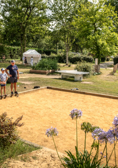 Famille jouant à la pétanque dans un parc de vacances en Occitanie, France, entourée de verdure et jeux.