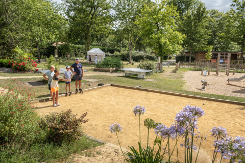 Familie spielt Boule auf dem Platz im Ferienpark in Occitanie, Frankreich, von Natur umgeben.