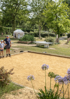 Familie spielt Boule auf dem Platz im Ferienpark in Occitanie, Frankreich, von Natur umgeben.