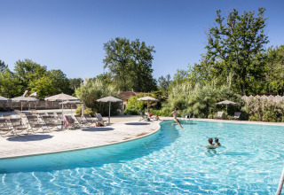 Udendørs swimmingpool ved Huttopia Lac de l'Uby - Gers feriepark, omgivet af træer og liggestole.