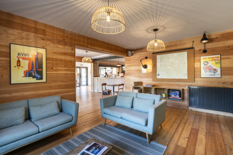 Relaxed lounge area at Huttopia Lac de l'Uby, Gers, with light sofas and wood walls in Occitanie, France.