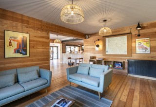 Relaxed lounge area at Huttopia Lac de l'Uby, Gers, with light sofas and wood walls in Occitanie, France.