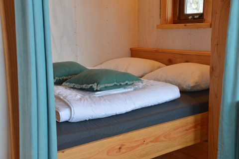Acogedora cama con almohadas y edredón en la casa del árbol Ooievaarsnest en Camping de Koeksebelt, Países Bajos.