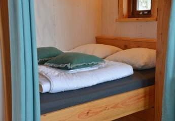 Letto accogliente con cuscini nella casa sull’albero Ooievaarsnest al Camping de Koeksebelt, Paesi Bassi.