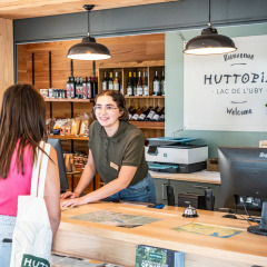 Rezeptionistin begrüßt Gast im Huttopia Lac de l'Uby, einem Ferienpark in Occitanie, Frankreich.