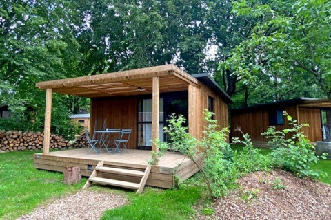 Cabaña Chalet Evasion de madera con porche, mobiliario exterior y rodeada de vegetación verde.