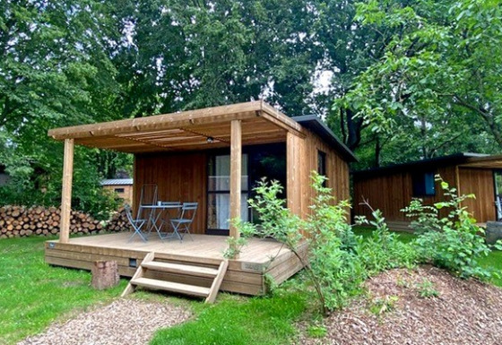 Cabaña Chalet Evasion de madera con porche, mobiliario exterior y rodeada de vegetación verde.