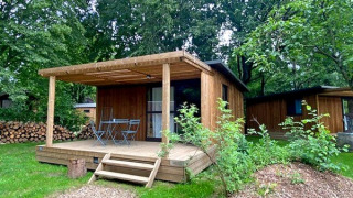 Holzhütte Chalet Evasion mit Veranda, Gartenmöbeln und umgeben von üppigem Grün und Bäumen.
