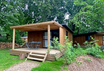 Chalet Evasion wooden cabin with a porch, outdoor chairs, table, and surrounded by lush greenery.