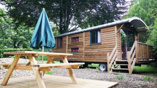 Gypsy caravan blokhut met houten terras, picknicktafel en parasol, midden in groene natuur.