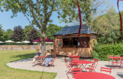 Udendørs caféområde med røde borde og stole ved en træhytte i Camping Valkenburg, Limburg, Holland.