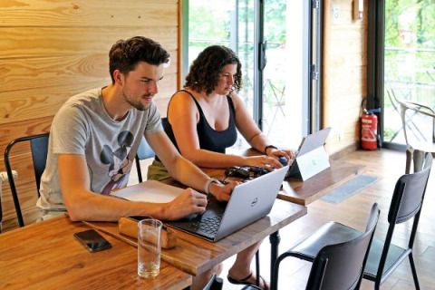 Dos jóvenes adultos trabajan en sus portátiles en Camping Valkenburg - Maastricht, parque vacacional en Limburgo.