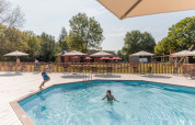 To børn leger i swimmingpoolen på Camping Valkenburg - Maastricht, omgivet af parasoller og grønne træer.