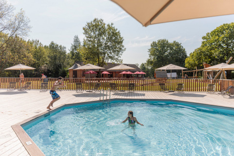 Niños jugando en la piscina del Camping Valkenburg - Maastricht, rodeados de sombrillas y vegetación.