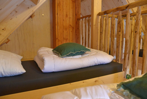 Lit de cabane dans les arbres avec couette blanche et coussin vert à Ooievaarsnest, Camping de Koeksebelt, Pays-Bas.