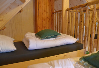 Lit de cabane dans les arbres avec couette blanche et coussin vert à Ooievaarsnest, Camping de Koeksebelt, Pays-Bas.