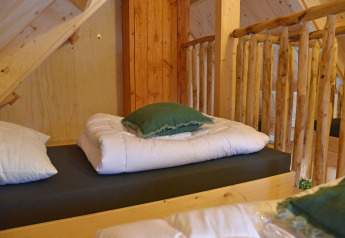 Boomhutbed met witte dons en groen kussen in Ooievaarsnest op Camping de Koeksebelt, Nederland.