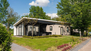 Moderna Bos Lodge en Holiday Resort 't Schuttenbelt, Países Bajos, rodeada de césped y árboles frondosos.