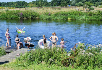 Bambini e adulti si divertono a nuotare e giocare con ciambelle gonfiabili in riva a un fiume verde.