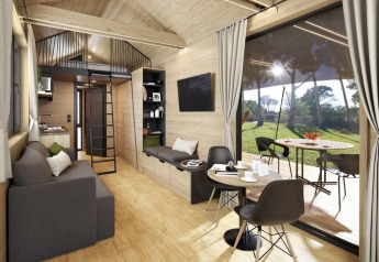 Acogedora casa pequeña con sofá, comedor, altillo y gran ventana con vistas al jardín en Bélgica.