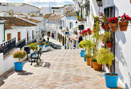 Calle empedrada en una pintoresca aldea blanca con macetas de flores y bancos bajo la luz del sol.