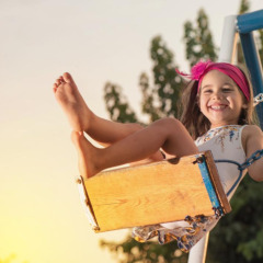 Niña feliz con diadema rosa juega en un columpio al atardecer en parque vacacional con glamping.