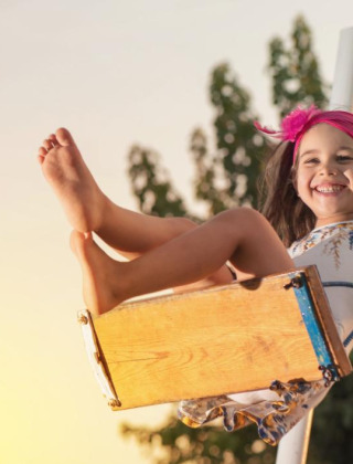 Niña feliz con diadema rosa juega en un columpio al atardecer en parque vacacional con glamping.