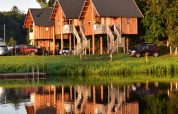Treehouses on stilts by the lakeside at Camping de Koeksebelt, Netherlands, reflected in calm water.