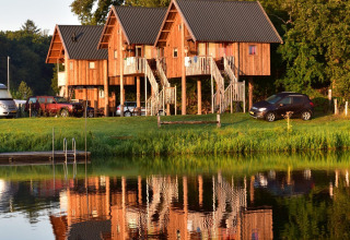 Baumhäuser auf Stelzen am See bei Camping de Koeksebelt, Niederlande, spiegeln sich im Wasser.