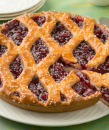 Primer plano de una tarta de cereza enrejada en plato blanco, servida en un parque vacacional con glamping.