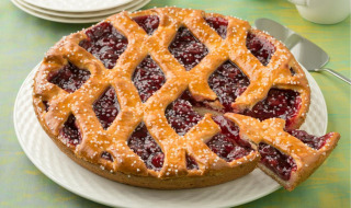 Primer plano de una tarta de cereza enrejada en plato blanco, servida en un parque vacacional con glamping.